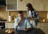 Couple looking stressed over bills at kitchen table.