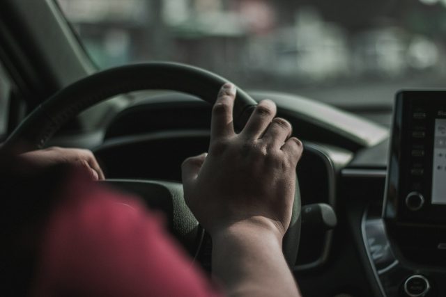 Photo by Mae Dulay a person driving a car with their hand on the steering wheel