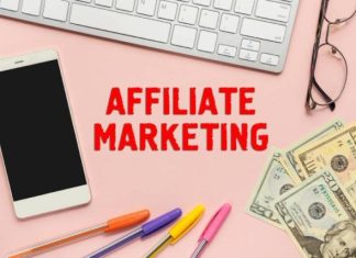 Evolution of Affiliate Programs in iGaming Flat lay of a smartphone, a keyboard, eyeglasses, colorful pens, and U.S. dollar bills on a pink background with the text 'Affiliate Marketing' in bold red letters. This image represents the concept of affiliate marketing, online income, and digital business opportunities.