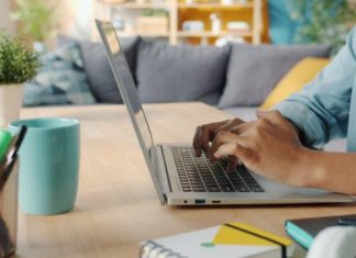 Person typing on a laptop at a wooden desk.
