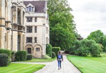person walking on concrete road beside brown concrete house near green high trees under white sky during daytime