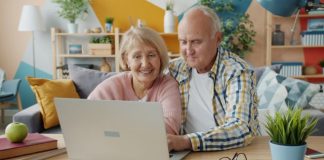 Elderly couple smiling while looking at laptop together.