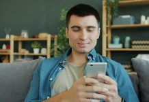Best Website for NSFW Chat: Why My Dream Companion Feels Too Real to Be Code Man smiling while holding a smartphone on a couch.