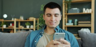 Man smiling while holding a smartphone on a couch.