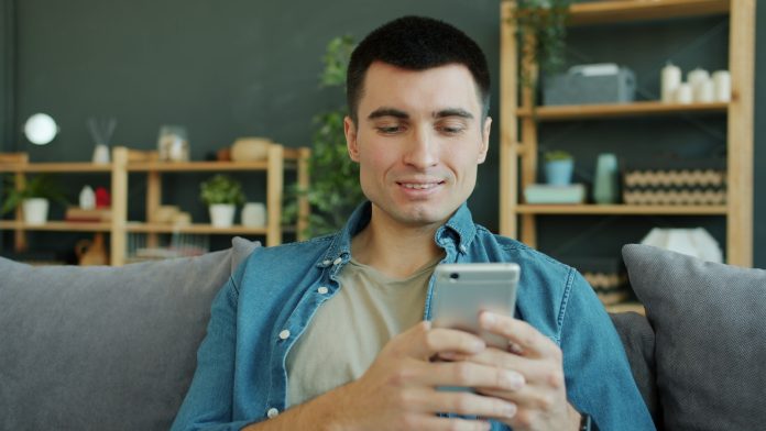 Man smiling while holding a smartphone on a couch.
