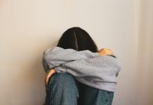 Five Ways Loneliness Can Increase the Risk of Addiction a woman sitting on the floor with her arms wrapped around her head