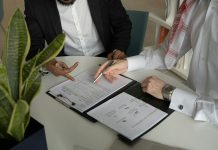 two men sitting at a table with papers and a pen