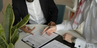 two men sitting at a table with papers and a pen