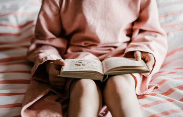 Photo by Annie Spratt person reading book sitting on red and white striped bedspread
