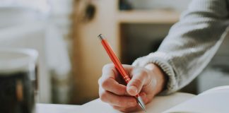 person holding on red pen while writing on book