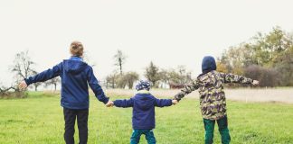 three children holding hands standing on grasses