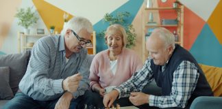 Three seniors playing chess together in a living room.
