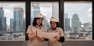Two women in hard hats review blueprints indoors.