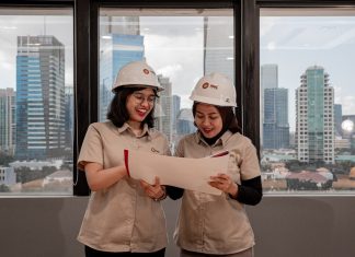 Two women in hard hats review blueprints indoors.