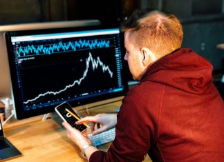man holding black smartphone with flat screen monitor in front