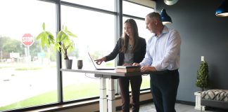 a man and a woman standing at a desk in front of a window