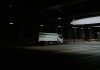 White delivery truck driving under a dark overpass.