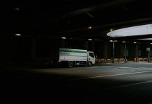 White delivery truck driving under a dark overpass.