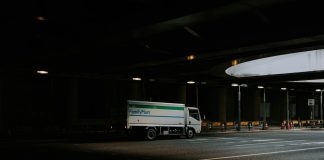 White delivery truck driving under a dark overpass.