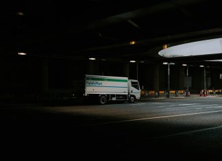 White delivery truck driving under a dark overpass.