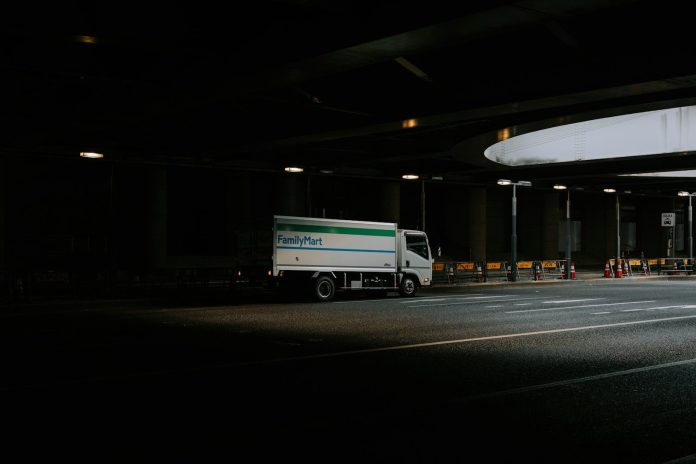 White delivery truck driving under a dark overpass.