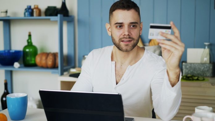 Photo by Vitaly Gariev Man holding credit card while looking at laptop