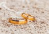 two gold wedding rings laying on the sand