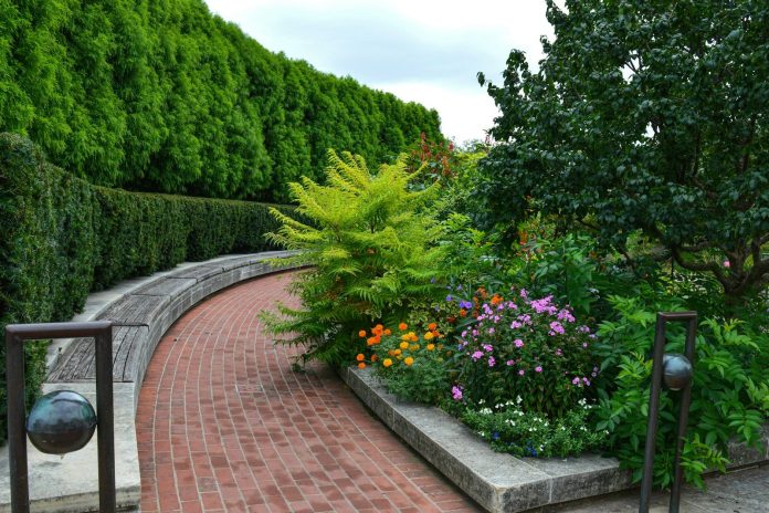 Photo by Annie Tray-Gavin a brick path with a garden of flowers and trees