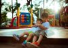 boy carrying child while sitting on gray concrete platform