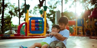 boy carrying child while sitting on gray concrete platform