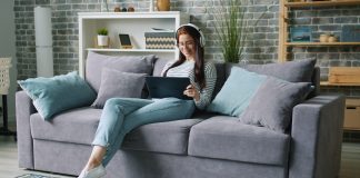 Woman wearing headphones uses tablet on couch.