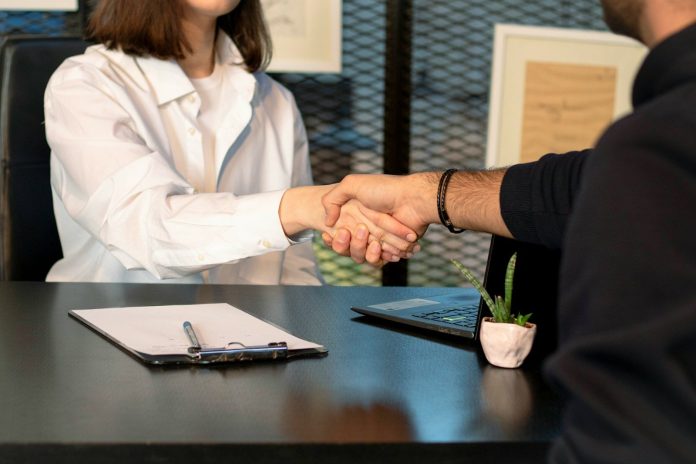 Photo by Mina Rad a man and a woman shaking hands in front of a laptop
