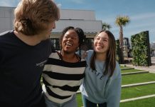 Three friends laughing together outdoors on a sunny day