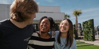 Three friends laughing together outdoors on a sunny day