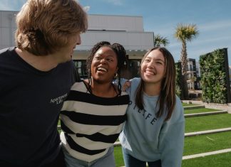 Three friends laughing together outdoors on a sunny day