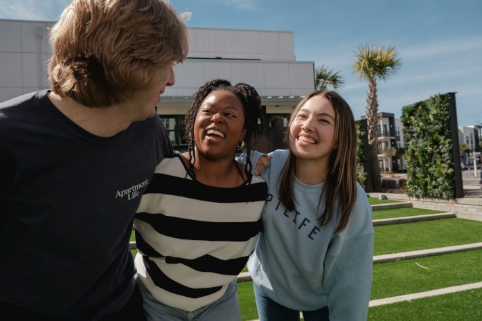 Three friends laughing together outdoors on a sunny day