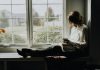 A woman sitting on a window sill reading a book