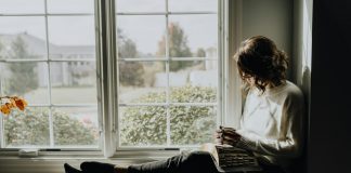 A woman sitting on a window sill reading a book