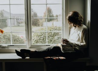 A woman sitting on a window sill reading a book