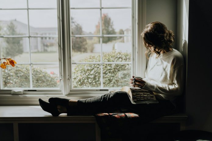 Photo by Kelly Sikkema A woman sitting on a window sill reading a book