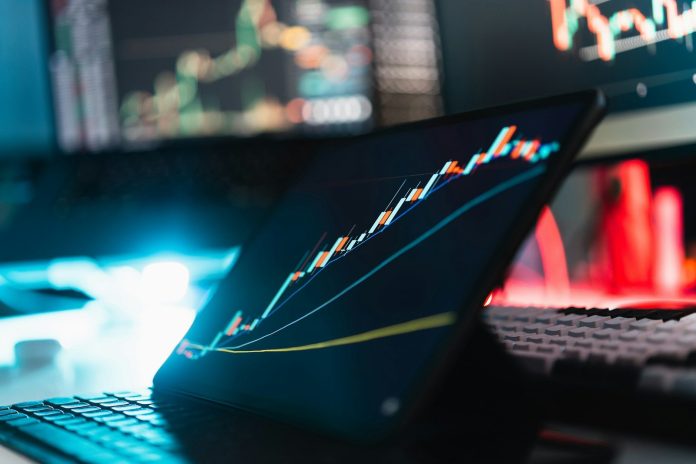 Photo by Jakub Żerdzicki A tablet displaying a rising stock market graph on a desk with a keyboard