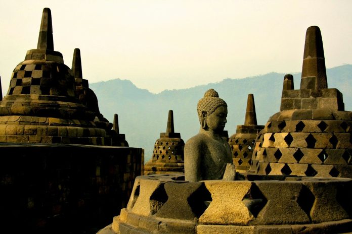 Photo by Mario La Pergola A stone Buddha statue among bell-shaped stupas at Borobudur temple in Indonesia