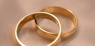 Two interlocking gold wedding bands on a textured cream fabric surface