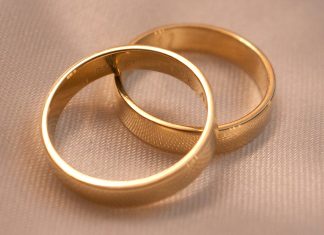 Two interlocking gold wedding bands on a textured cream fabric surface
