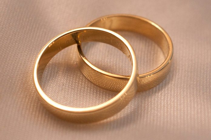 Photo by Mariano Rivas Two interlocking gold wedding bands on a textured cream fabric surface